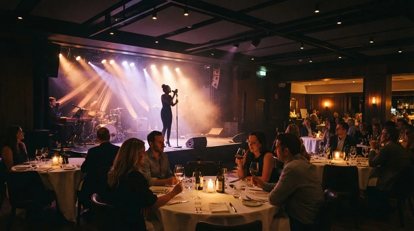 Escenario iluminado dentro de la sala de eventos del casino, con público sentado en mesas y copas sobre los manteles